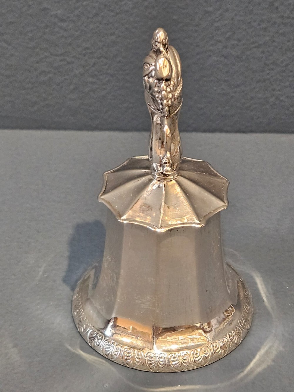 A Victorian silver table bell featuring a fruit basket finial, dual handles, a faceted body, and an embossed rim. View VI