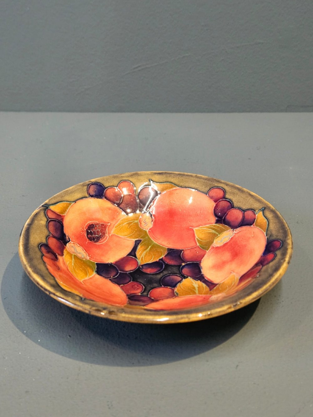 A circular shallow earthenware bowl decorated with hand-painted tubelined pomegranate fruits and dark berries over an ochre-tinted ground.