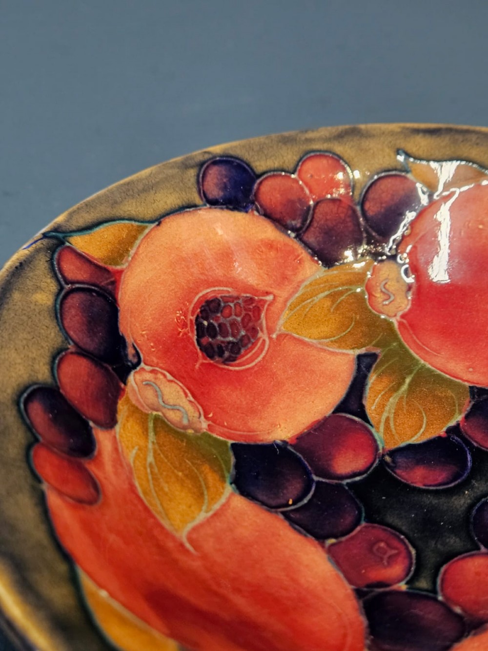 A circular shallow earthenware bowl decorated with hand-painted tubelined pomegranate fruits and dark berries over an ochre-tinted ground. View III