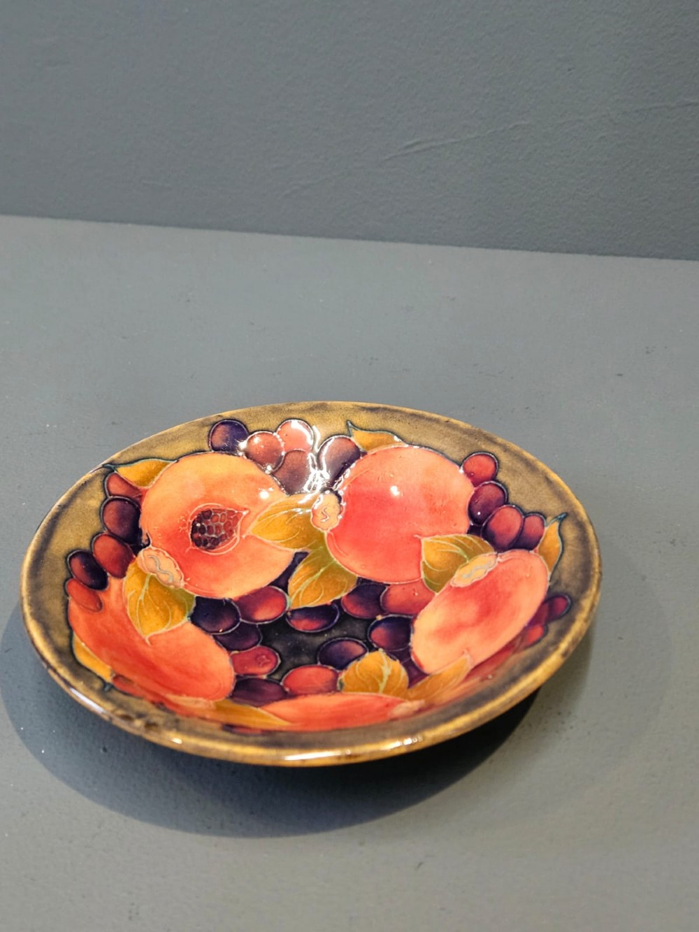 A circular shallow earthenware bowl decorated with hand-painted tubelined pomegranate fruits and dark berries over an ochre-tinted ground. View IV