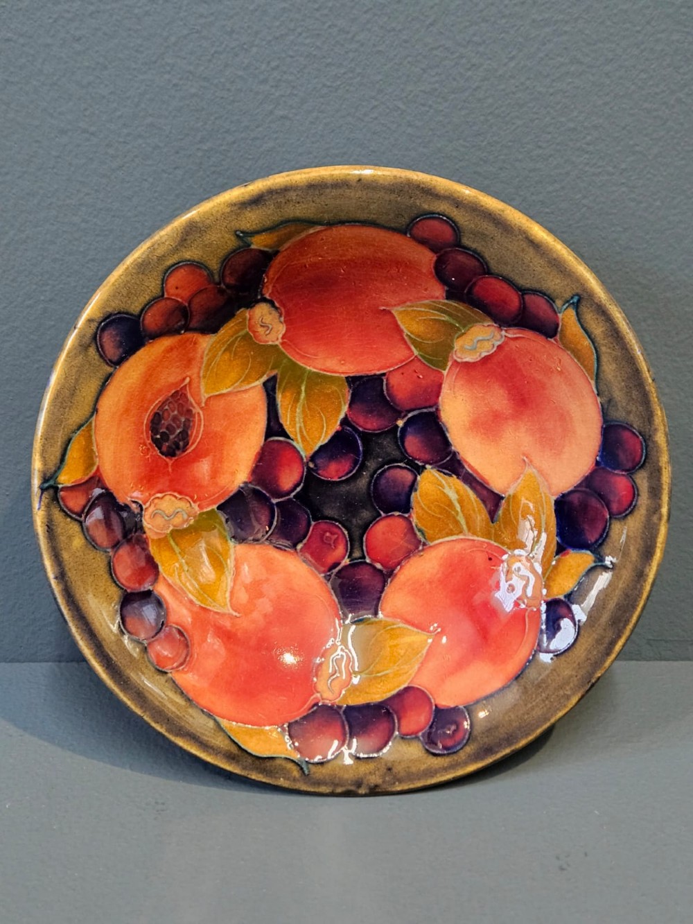 A circular shallow earthenware bowl decorated with hand-painted tubelined pomegranate fruits and dark berries over an ochre-tinted ground. View V