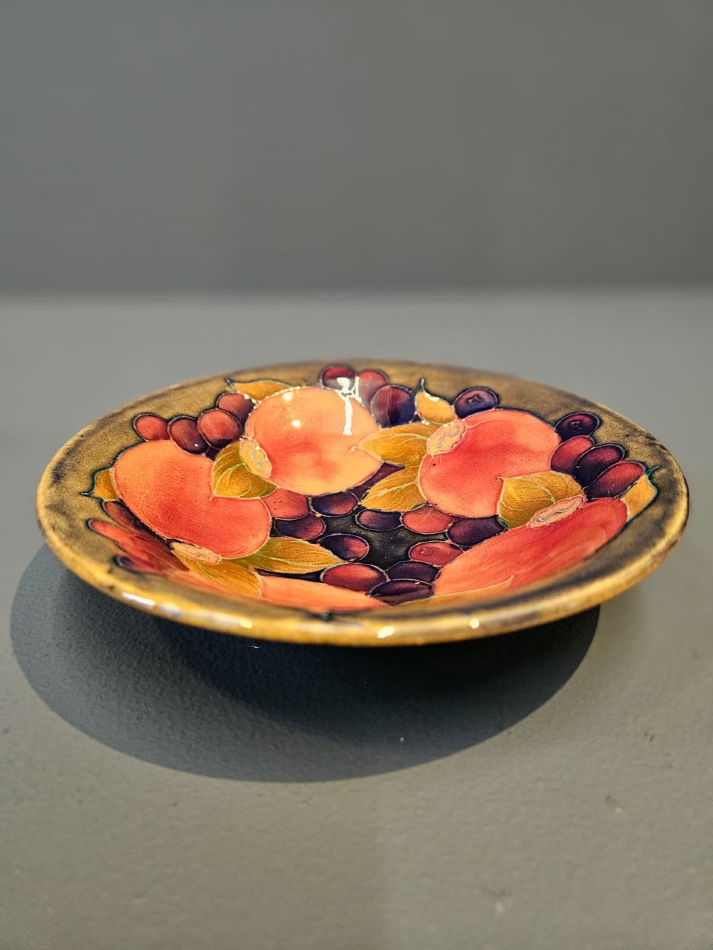 A circular shallow earthenware bowl decorated with hand-painted tubelined pomegranate fruits and dark berries over an ochre-tinted ground. View VII