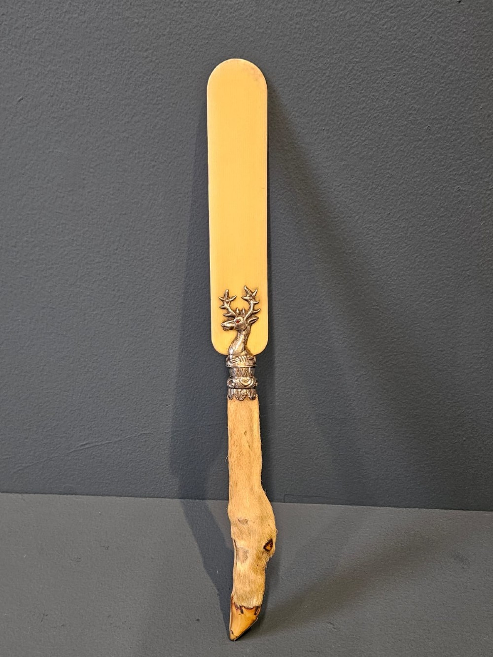 A Victorian page turner with a smooth cream blade, a silver deer motif at the base, and a taxidermy deer hoof handle.