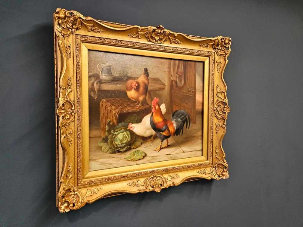 An oil painting on canvas depicting a cockerel and two hens inside a rustic barn beside a wicker basket and cabbage, enclosed in a heavily carved gold frame. View III