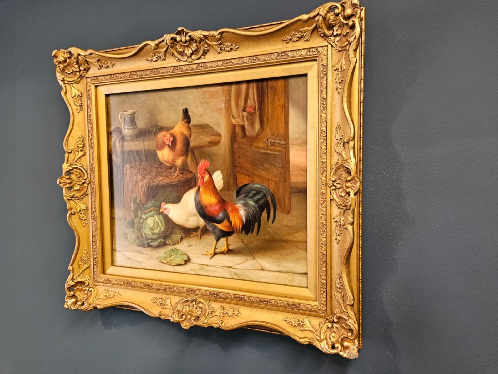 An oil painting on canvas depicting a cockerel and two hens inside a rustic barn beside a wicker basket and cabbage, enclosed in a heavily carved gold frame. View V