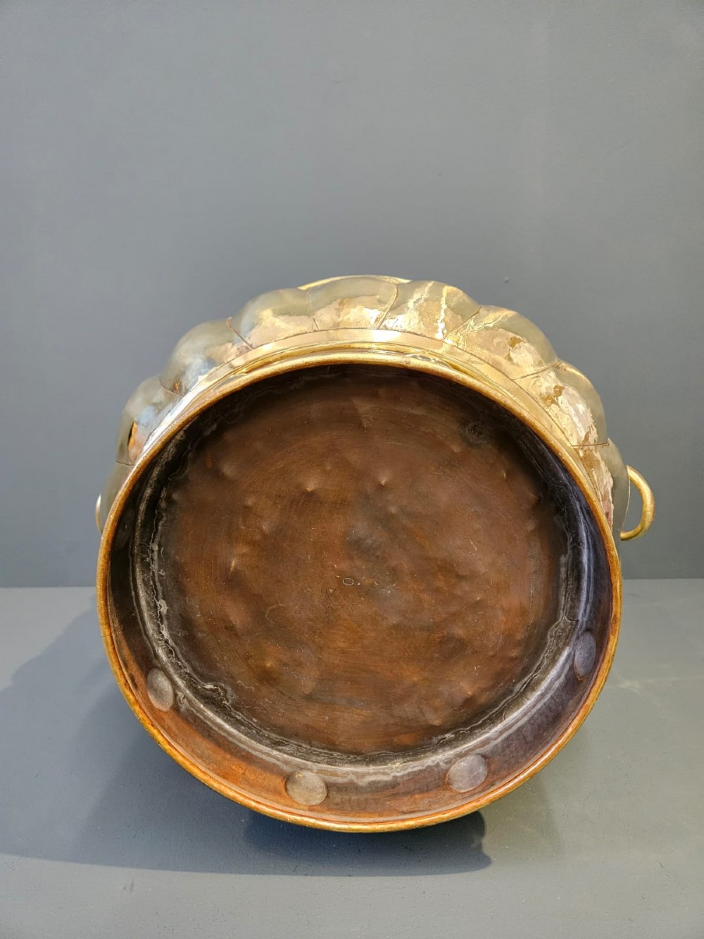 A large polished brass cylindrical planter with an embossed heraldic crest on the front, godrooned base pattern, and side ring handles. View II