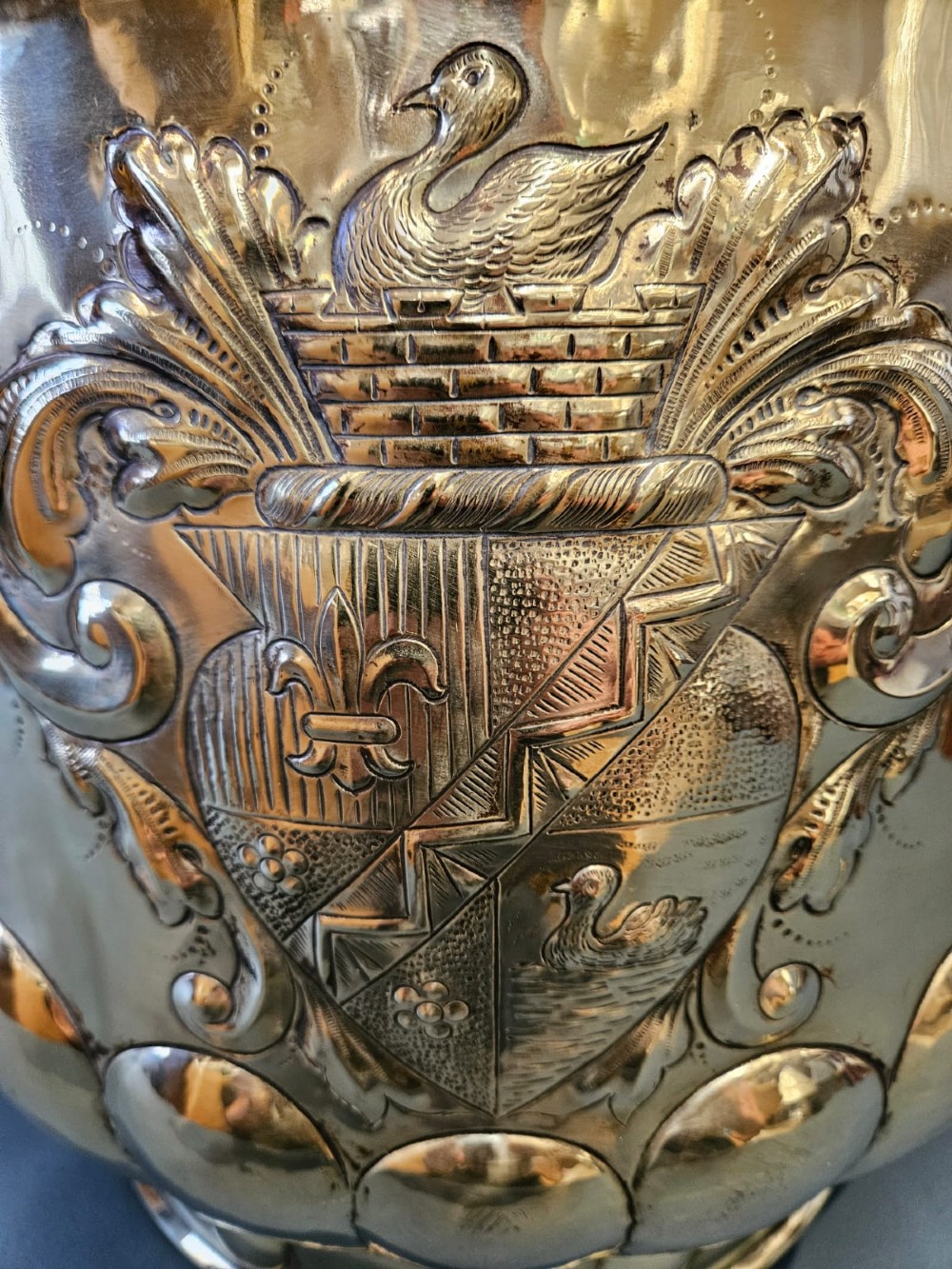 A large polished brass cylindrical planter with an embossed heraldic crest on the front, godrooned base pattern, and side ring handles. View V