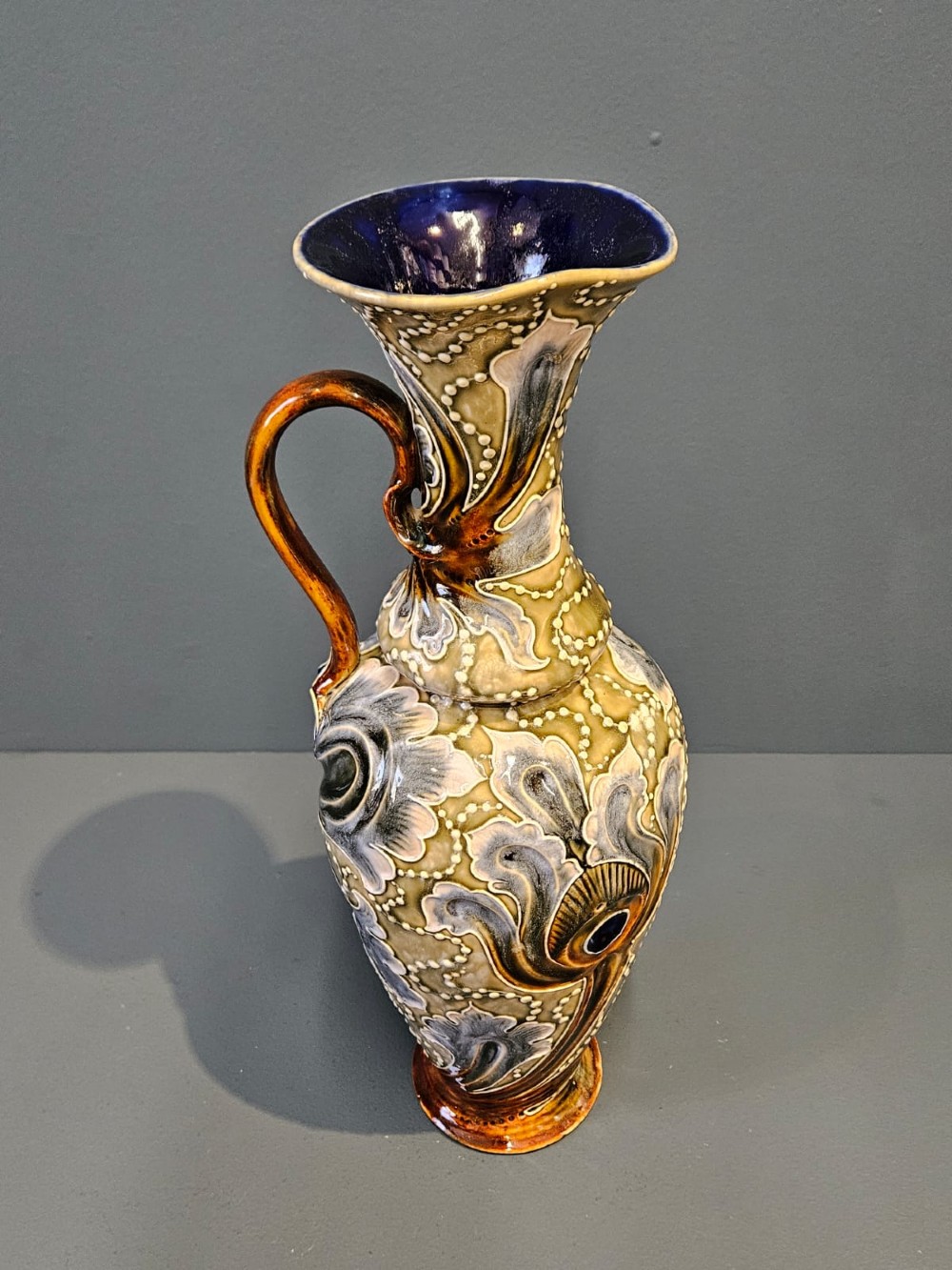 A tall Victorian Doulton Lambeth stoneware ewer decorated with incised leaf motifs, white beaded slipwork, an ochre handle, and a deep cobalt blue glazed interior.