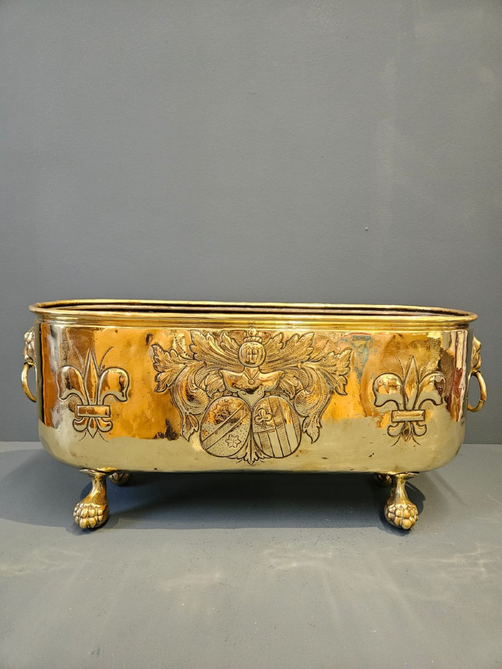 An oblong Victorian brass planter featuring an embossed armorial crest, fleur-de-lis motifs, side ring handles, and cast claw feet. View III