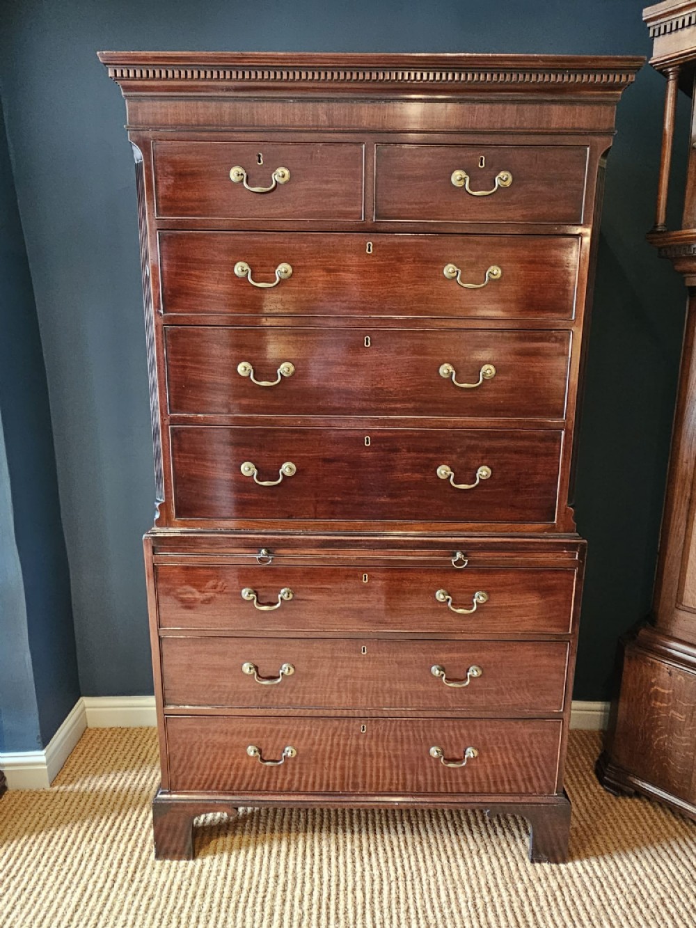 A George III mahogany chest on chest featuring two stacked drawer sections, swan-neck brass handles, dentil moulding, and bracket feet.