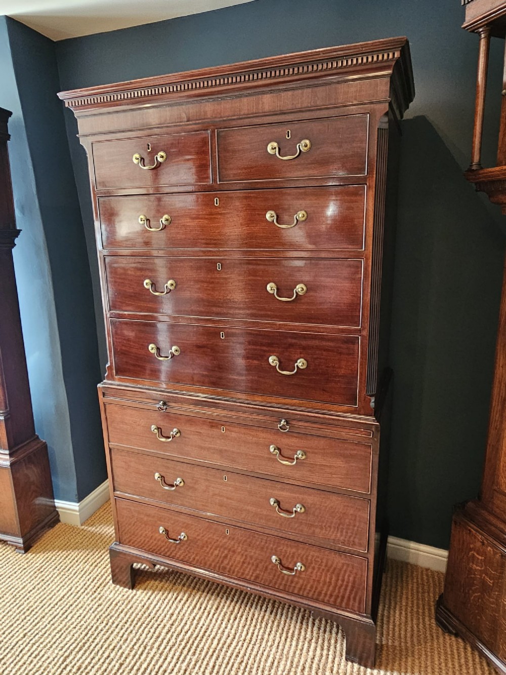 A George III mahogany chest on chest featuring two stacked drawer sections, swan-neck brass handles, dentil moulding, and bracket feet. View II