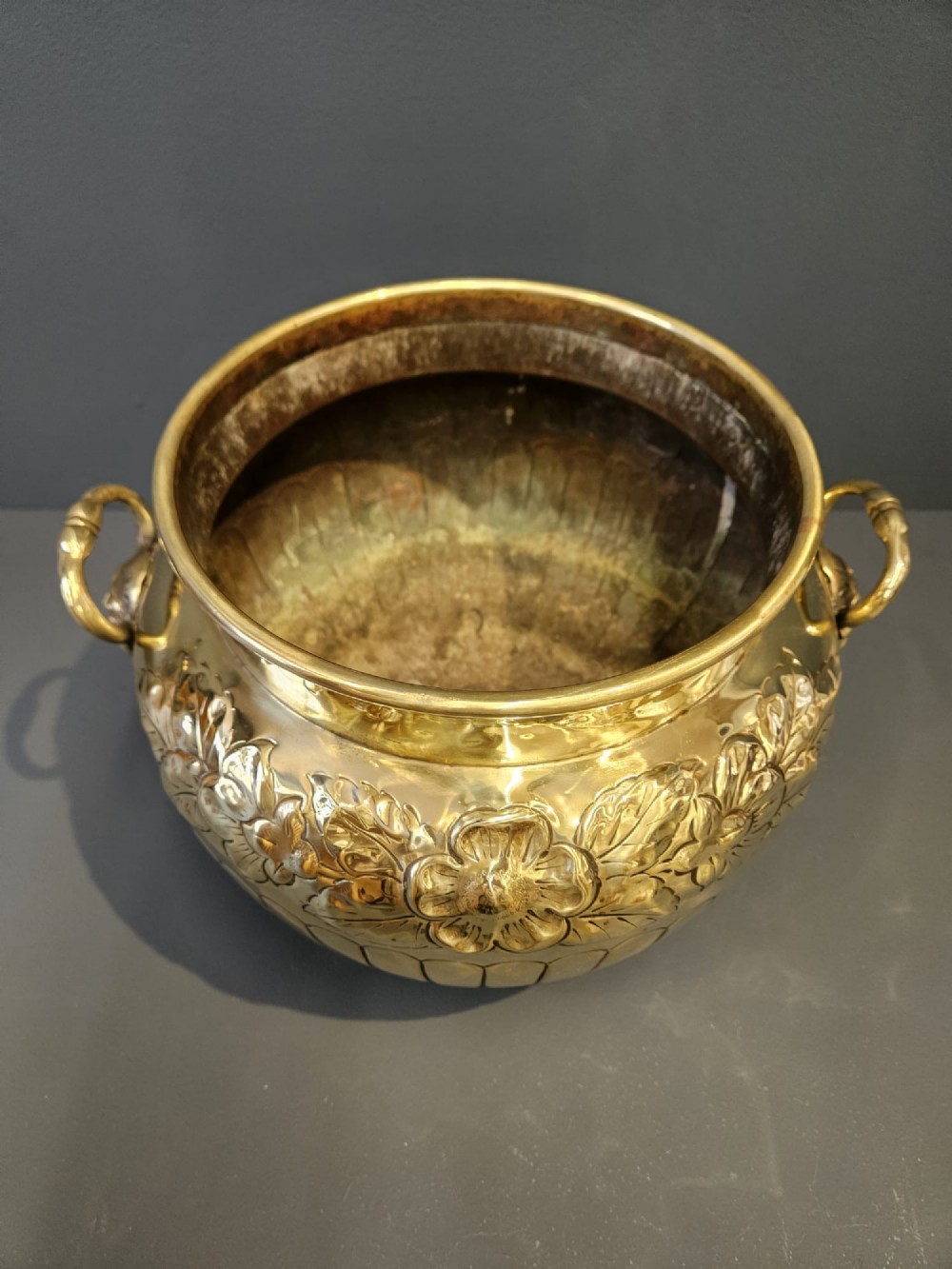 A polished Victorian brass jardiniere planter featuring embossed floral detailing around the upper band, fluted gadrooning on the lower body, and two side handles. View III