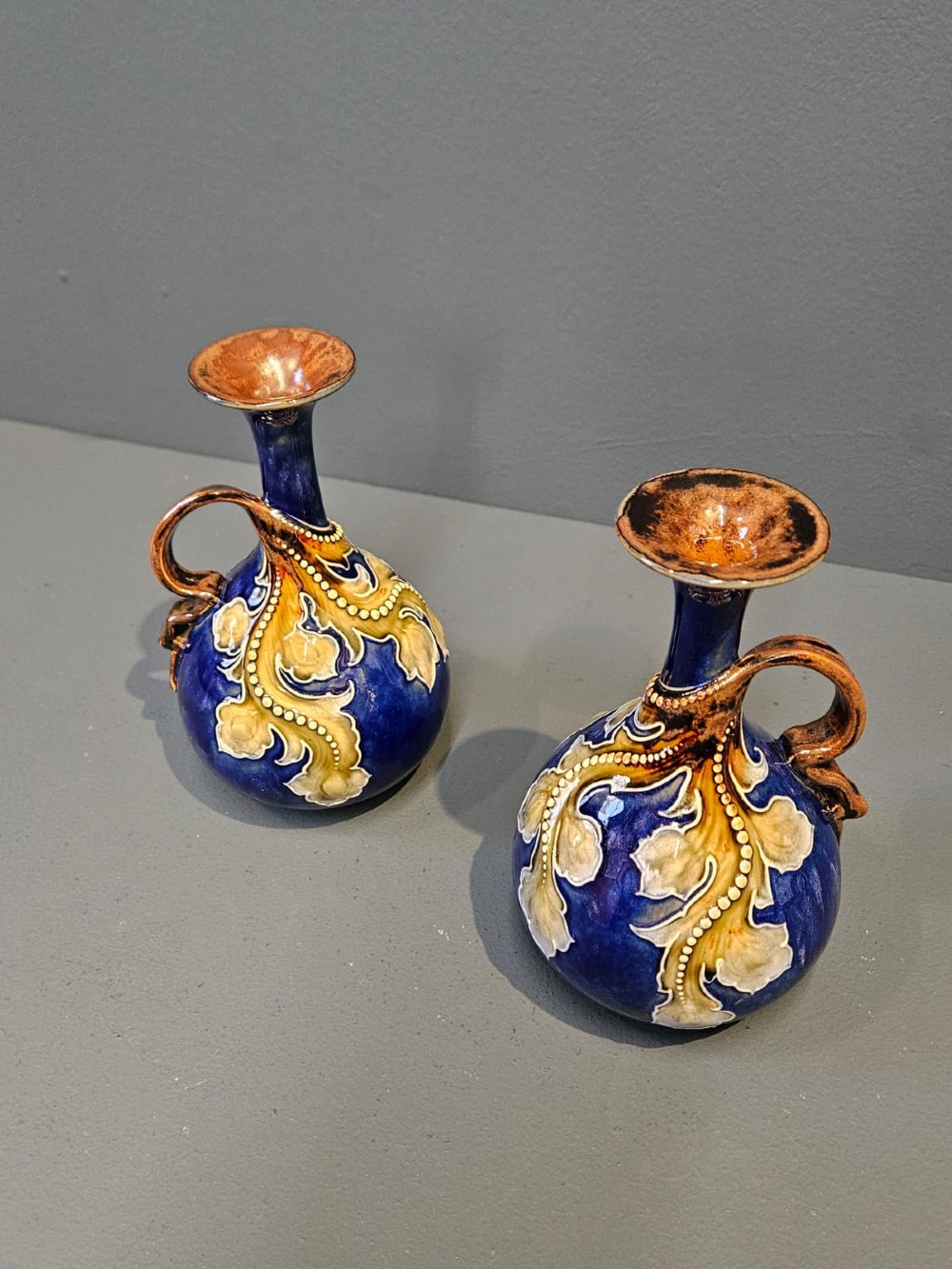 A pair of Victorian Doulton Lambeth stoneware ewers featuring cobalt blue glazed bodies, single handles, and raised foliage decoration in beige and ocher. View II