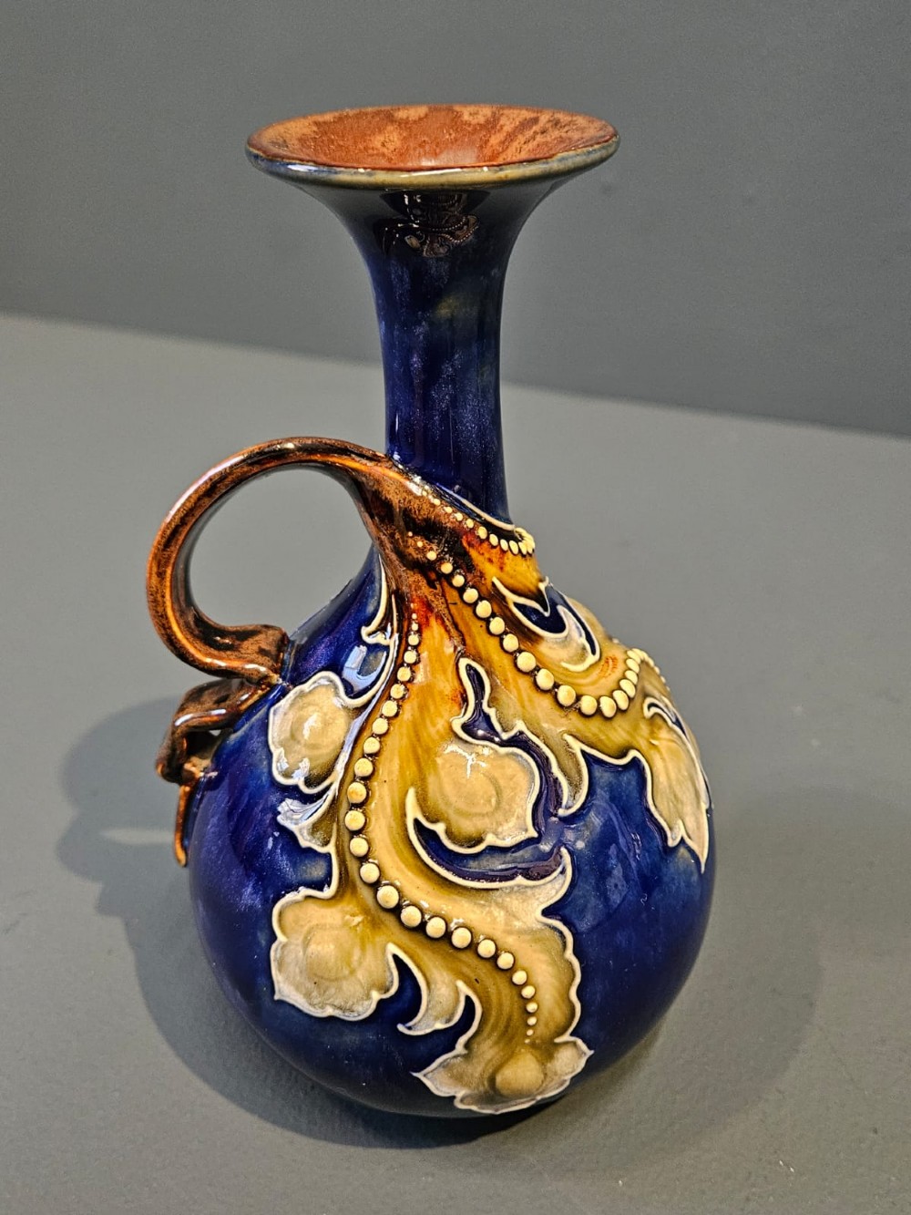 A pair of Victorian Doulton Lambeth stoneware ewers featuring cobalt blue glazed bodies, single handles, and raised foliage decoration in beige and ocher. View III