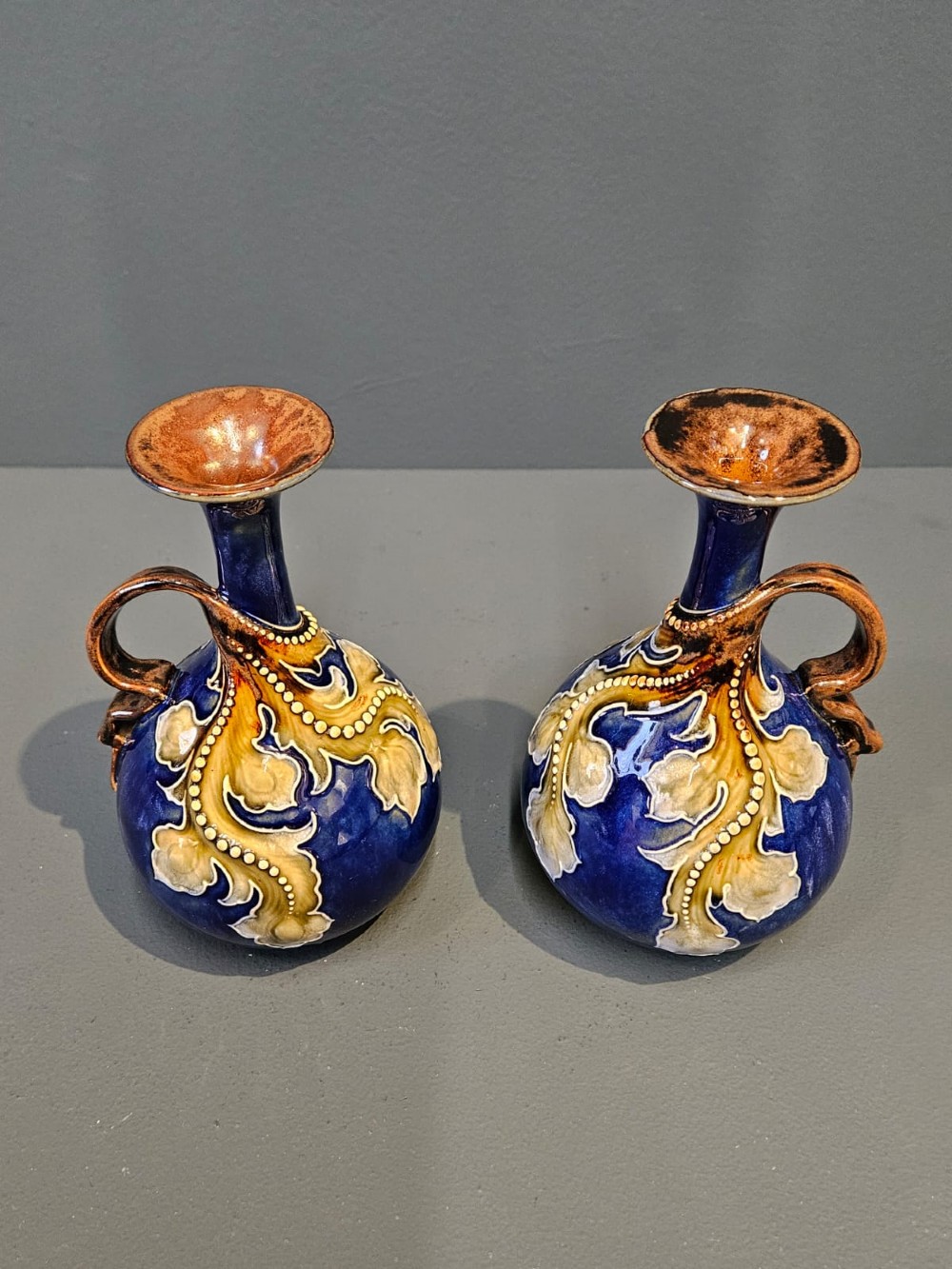 A pair of Victorian Doulton Lambeth stoneware ewers featuring cobalt blue glazed bodies, single handles, and raised foliage decoration in beige and ocher. View IV