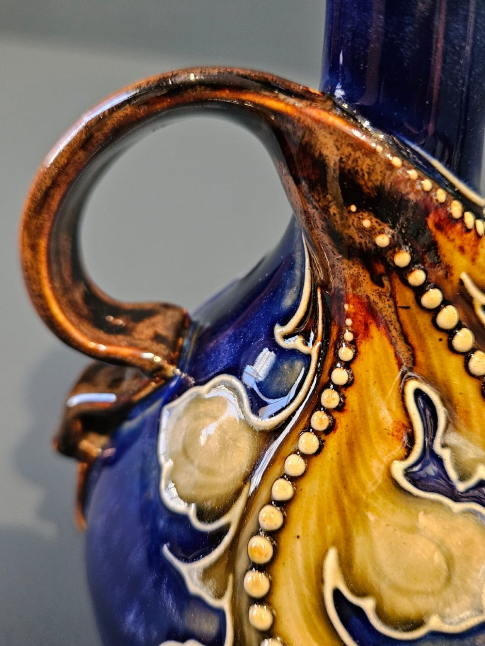 A pair of Victorian Doulton Lambeth stoneware ewers featuring cobalt blue glazed bodies, single handles, and raised foliage decoration in beige and ocher. View V