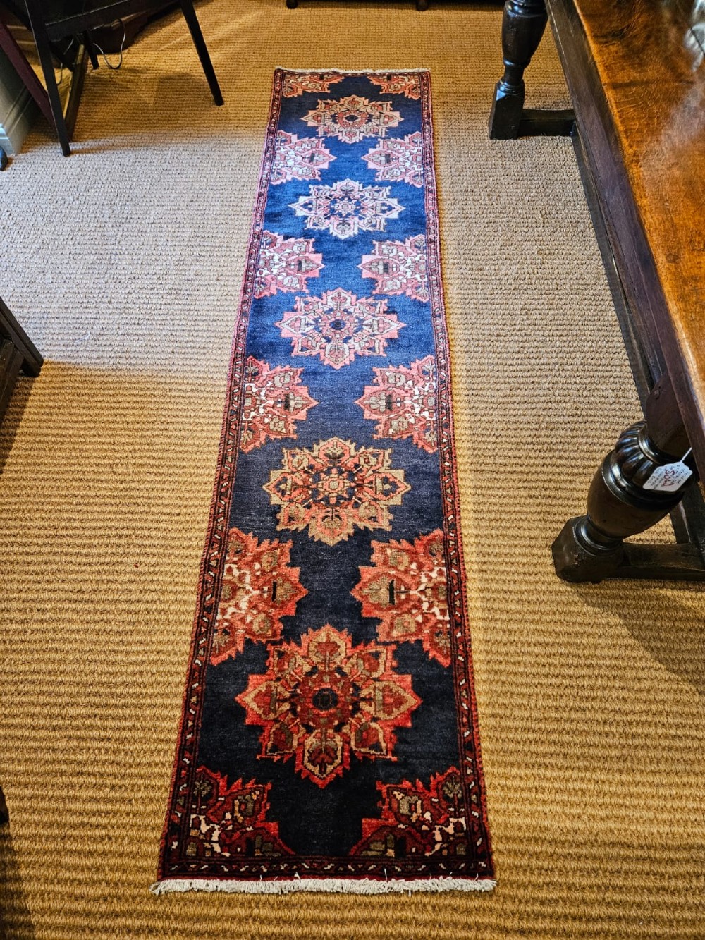 A long narrow navy blue runner rug decorated with a row of repeating geometric star medallions in terracotta and cream tones.