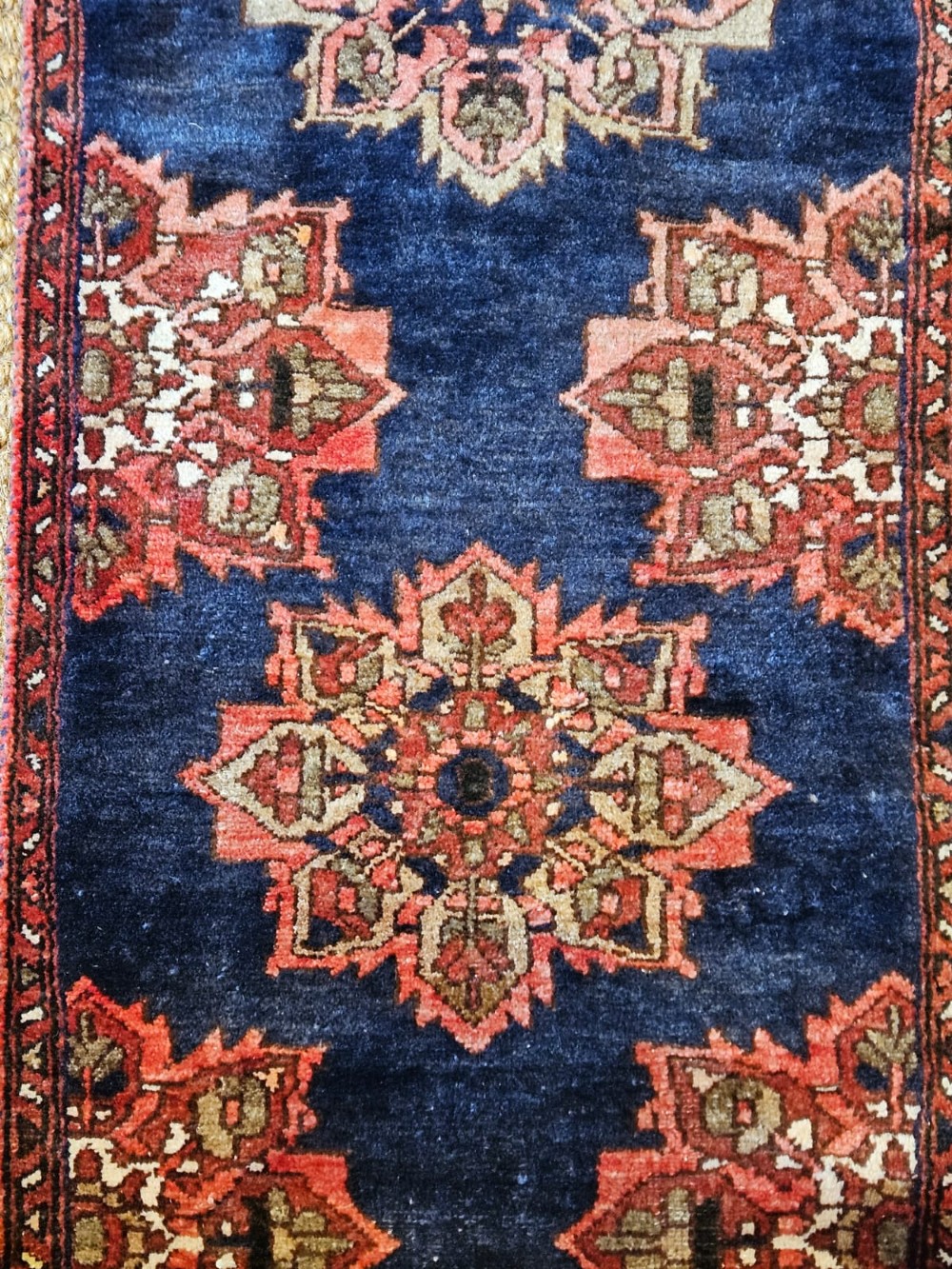 A long narrow navy blue runner rug decorated with a row of repeating geometric star medallions in terracotta and cream tones. View II