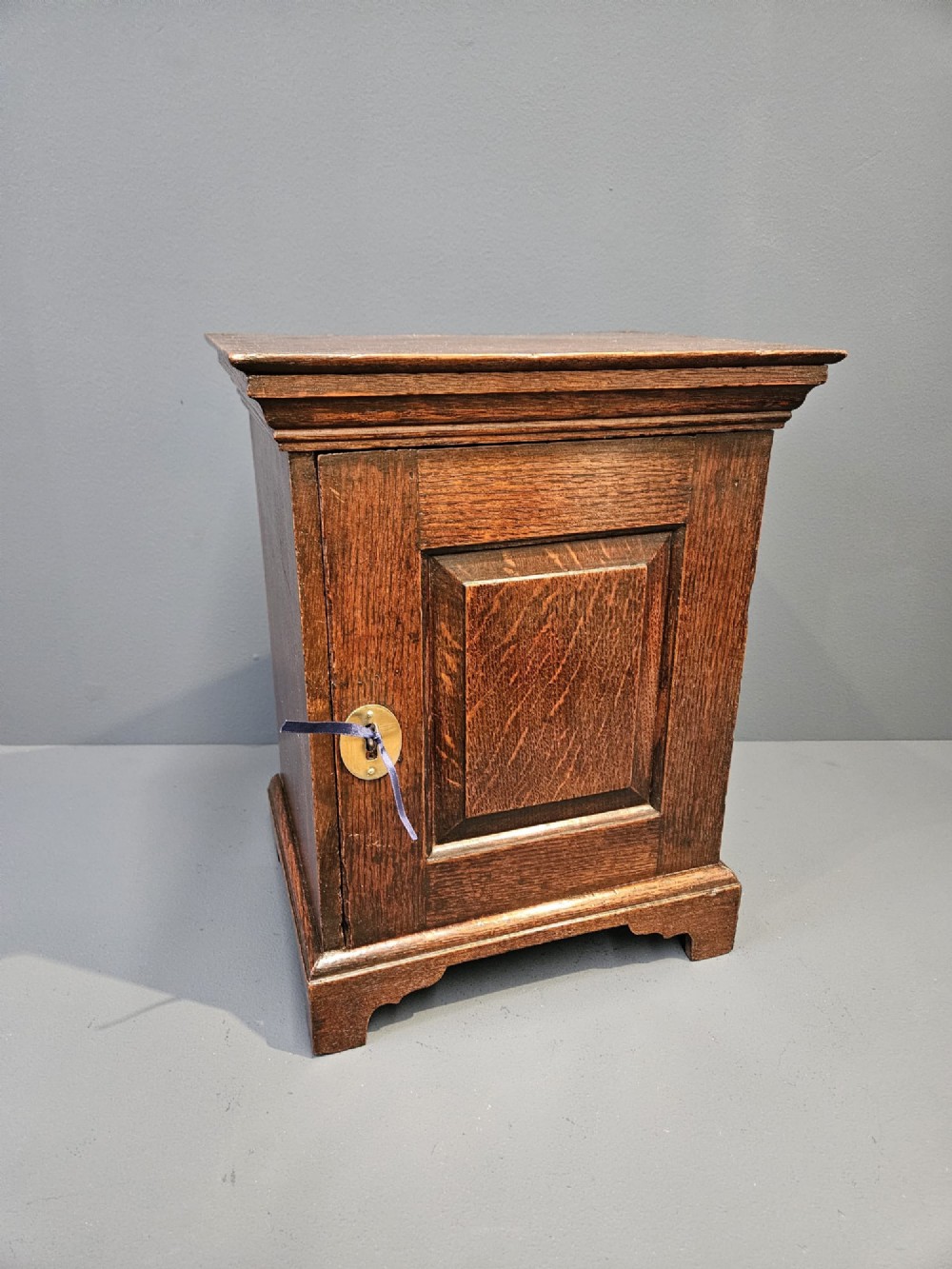 A George II dark oak spice cupboard with a moulded cornice, a single fielded-panel door, and a brass keyhole escutcheon.