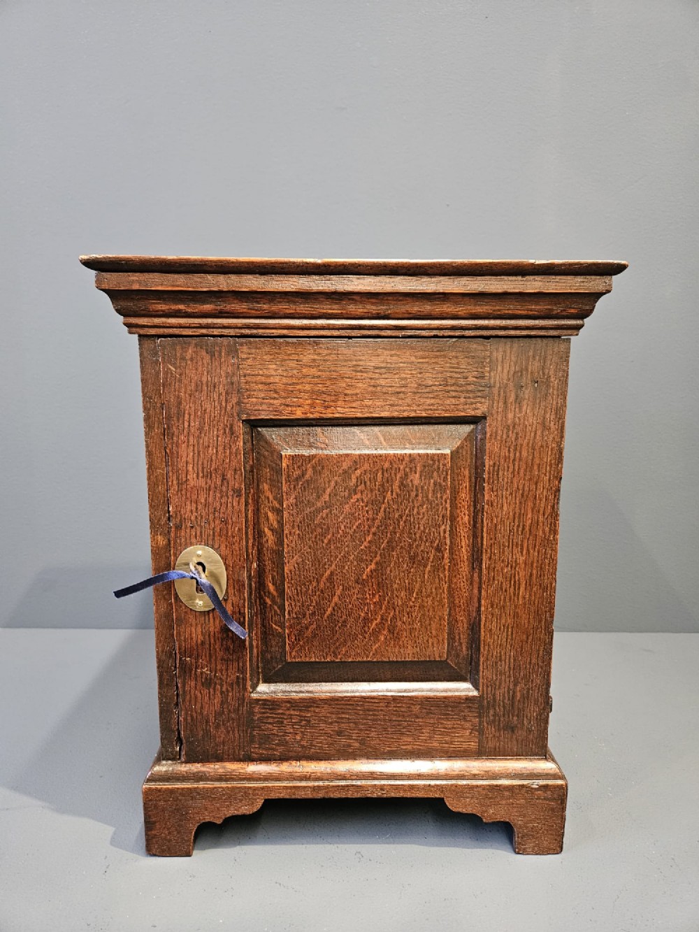 A George II dark oak spice cupboard with a moulded cornice, a single fielded-panel door, and a brass keyhole escutcheon. View III