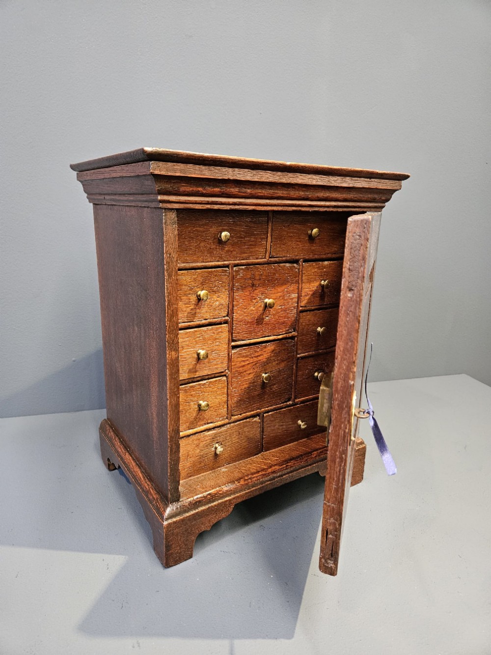 A George II dark oak spice cupboard with a moulded cornice, a single fielded-panel door, and a brass keyhole escutcheon. View V