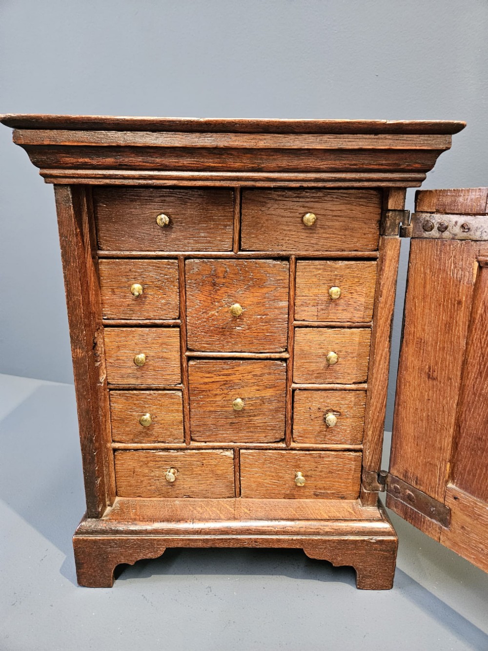 A George II dark oak spice cupboard with a moulded cornice, a single fielded-panel door, and a brass keyhole escutcheon. View VI