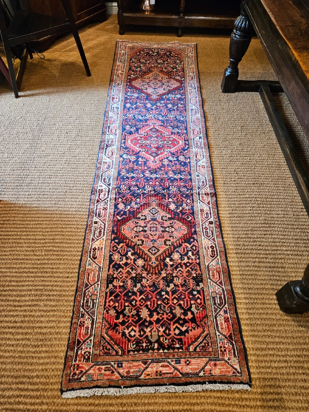 A long hand-knotted wool runner rug featuring deep navy blue and terracotta geometric medallion patterns with a cream decorated border.