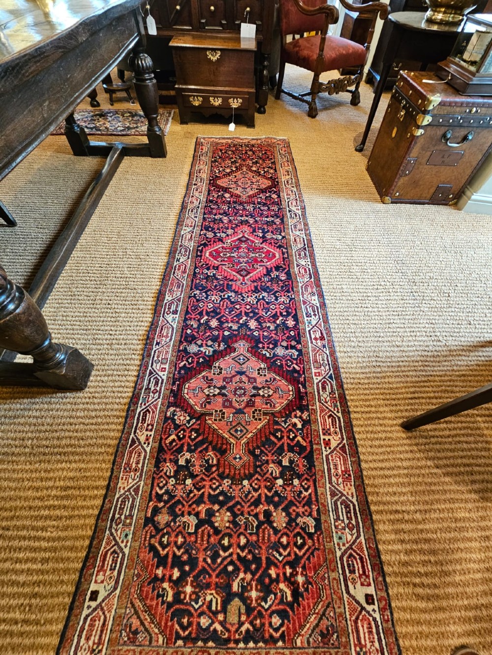 A long hand-knotted wool runner rug featuring deep navy blue and terracotta geometric medallion patterns with a cream decorated border. View V