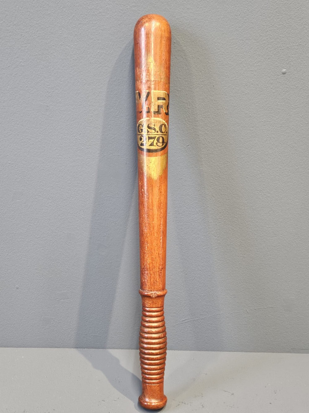 A turned Victorian mahogany police truncheon featuring a ribbed handle and painted VR royal cypher detailing on a warm brown shaft.