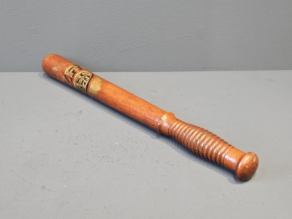 A turned Victorian mahogany police truncheon featuring a ribbed handle and painted VR royal cypher detailing on a warm brown shaft. View II