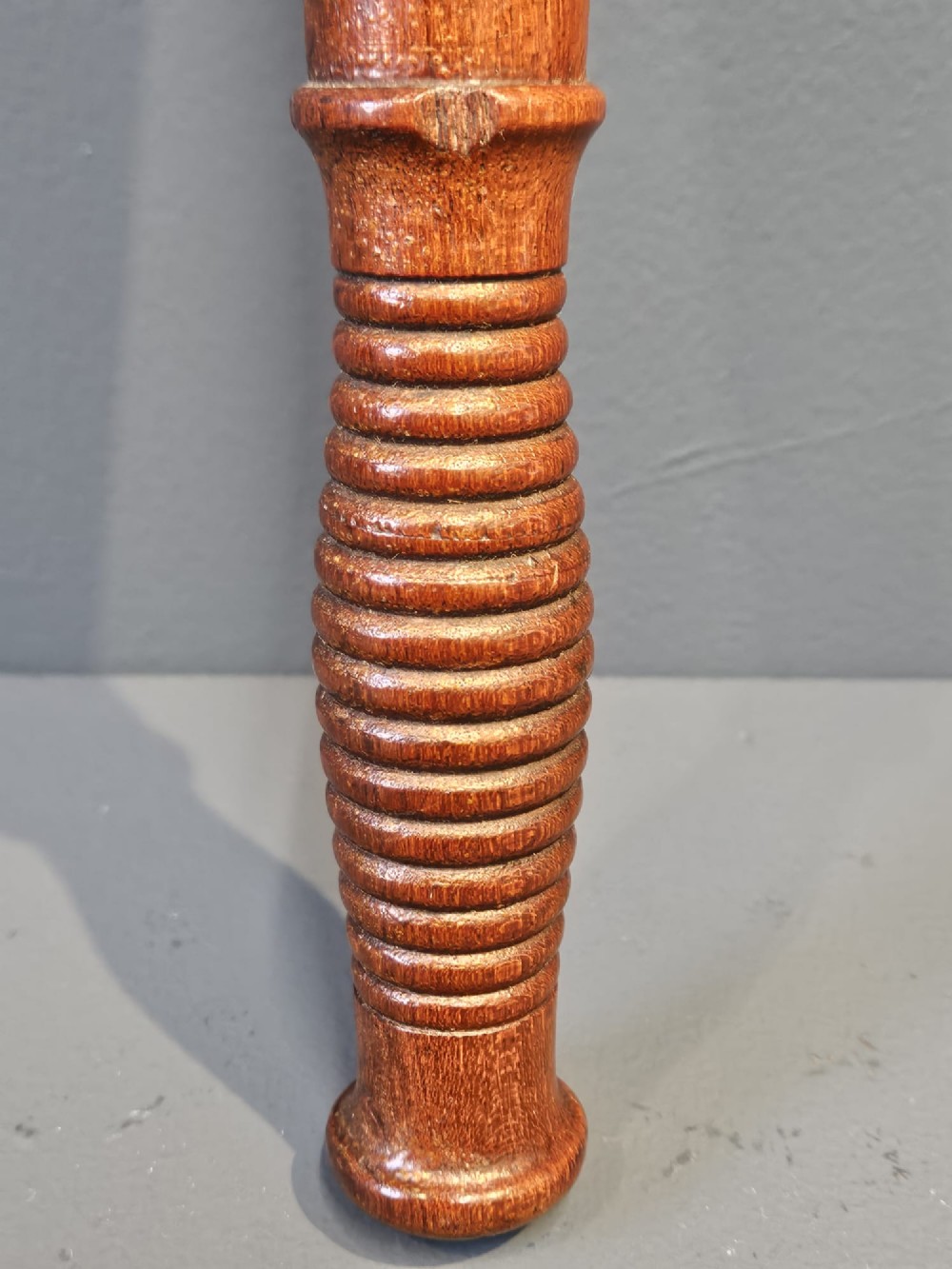 A turned Victorian mahogany police truncheon featuring a ribbed handle and painted VR royal cypher detailing on a warm brown shaft. View IV