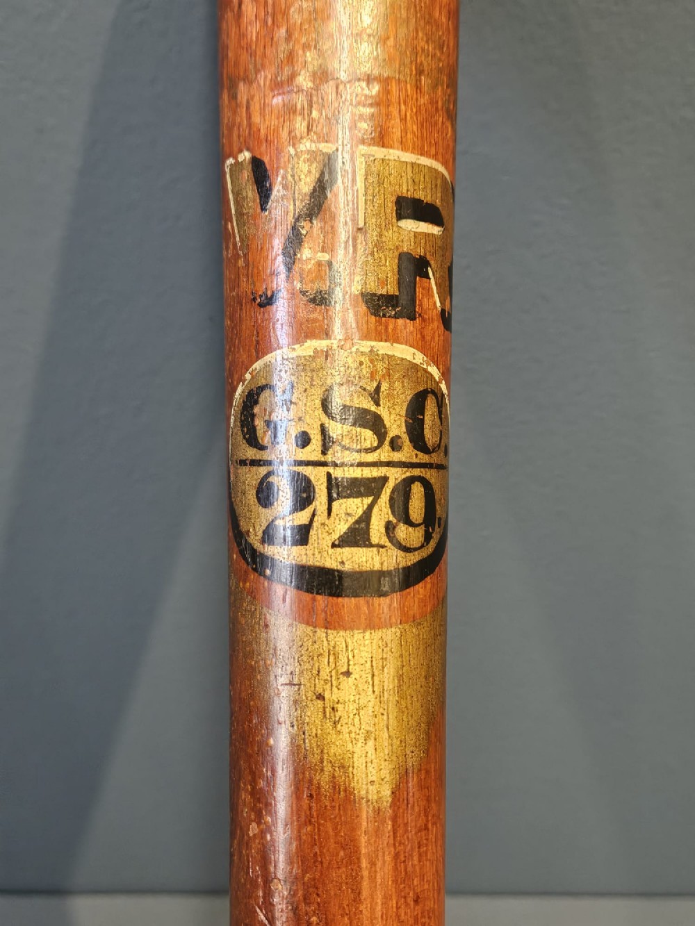 A turned Victorian mahogany police truncheon featuring a ribbed handle and painted VR royal cypher detailing on a warm brown shaft. View V