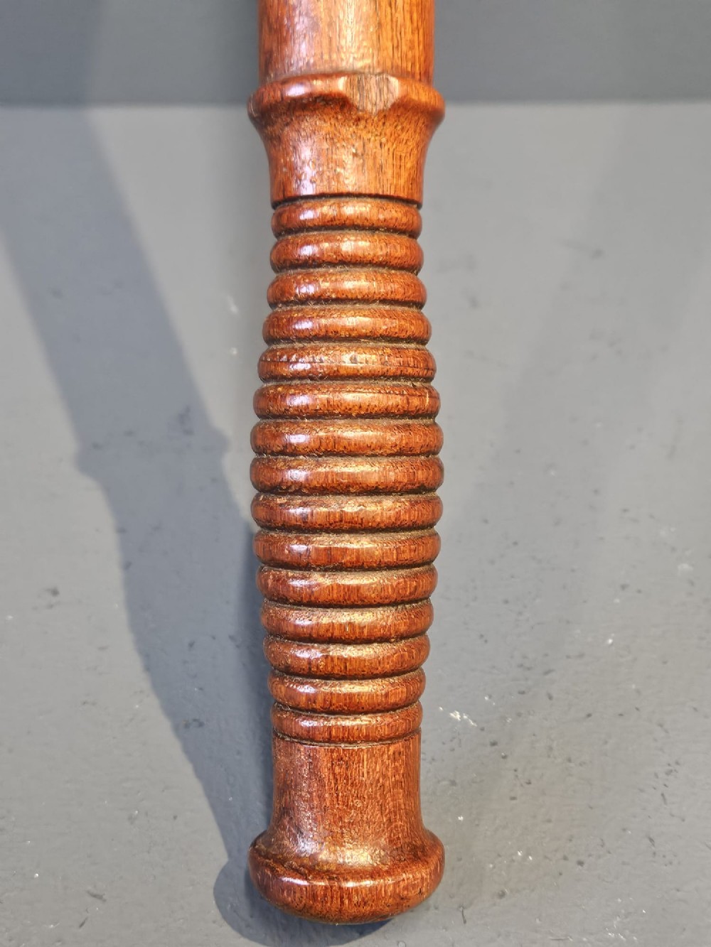 A turned Victorian mahogany police truncheon featuring a ribbed handle and painted VR royal cypher detailing on a warm brown shaft. View VI