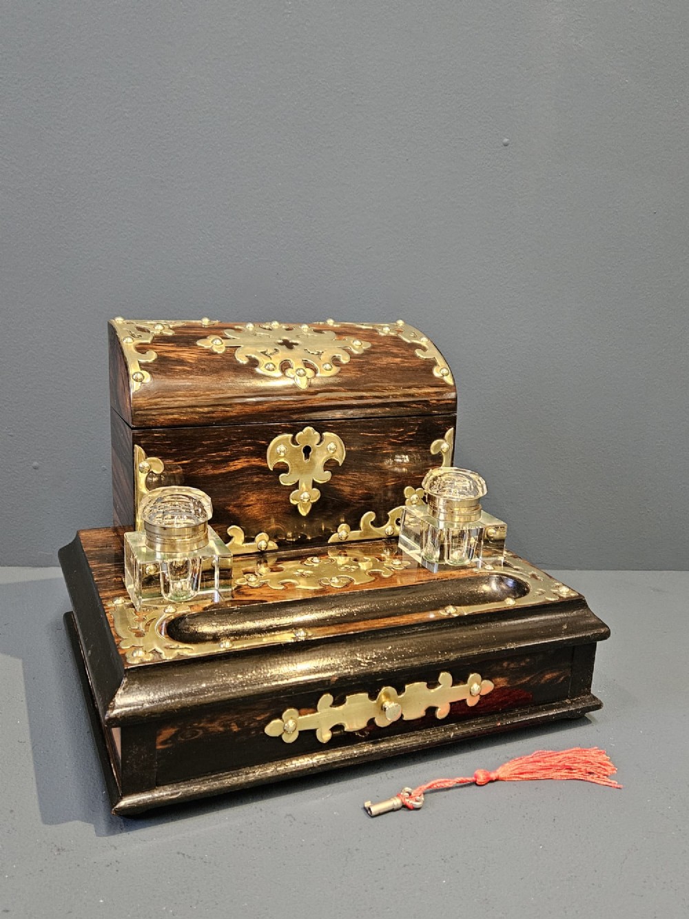 A Victorian coromandel wood stationery box and inkstand featuring gothic brass strapwork mounts, a domed lid, two glass inkwells, and a lower drawer with a key.