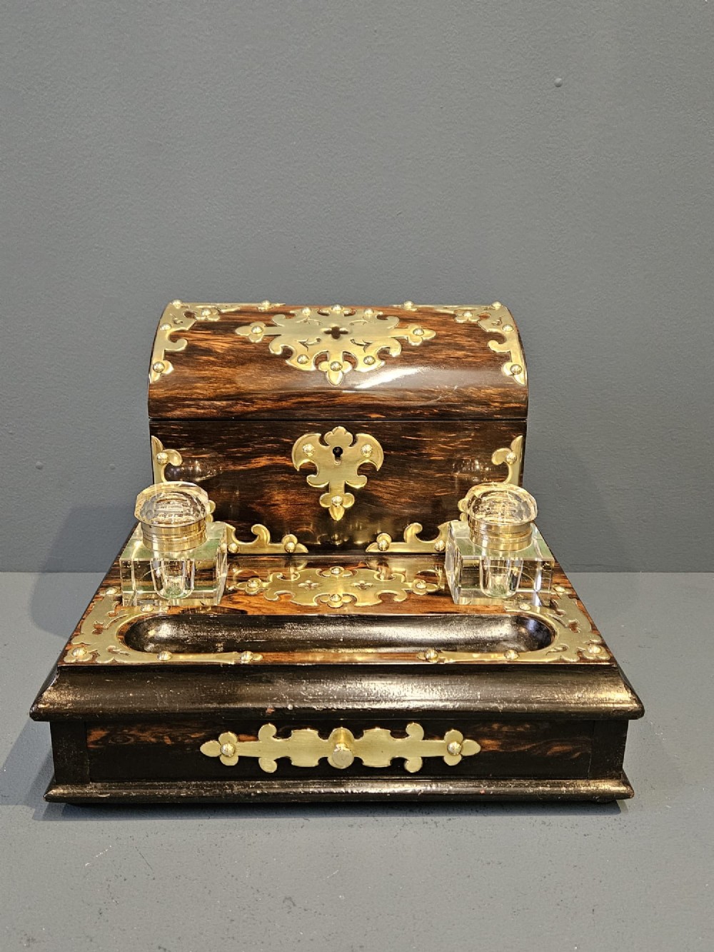 A Victorian coromandel wood stationery box and inkstand featuring gothic brass strapwork mounts, a domed lid, two glass inkwells, and a lower drawer with a key. View II