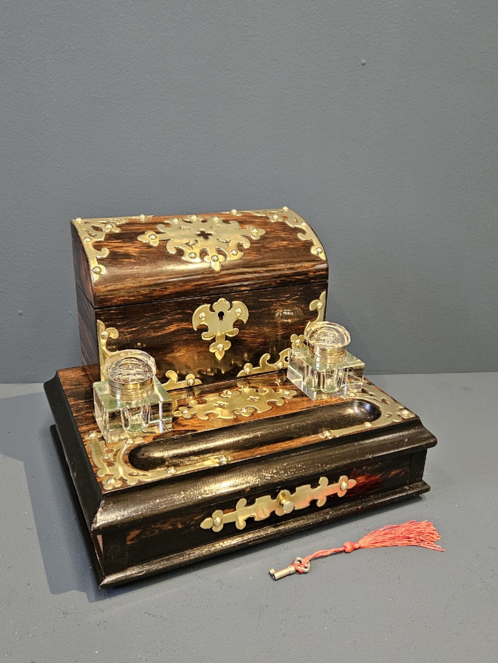 A Victorian coromandel wood stationery box and inkstand featuring gothic brass strapwork mounts, a domed lid, two glass inkwells, and a lower drawer with a key. View III