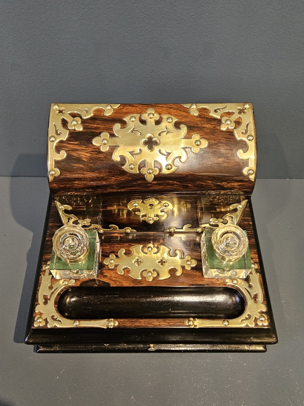 A Victorian coromandel wood stationery box and inkstand featuring gothic brass strapwork mounts, a domed lid, two glass inkwells, and a lower drawer with a key. View IV