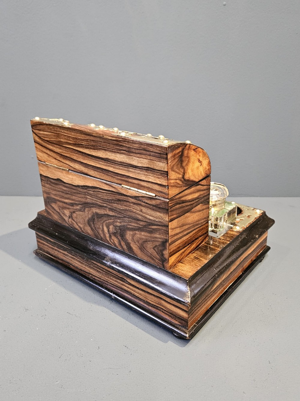 A Victorian coromandel wood stationery box and inkstand featuring gothic brass strapwork mounts, a domed lid, two glass inkwells, and a lower drawer with a key. View V