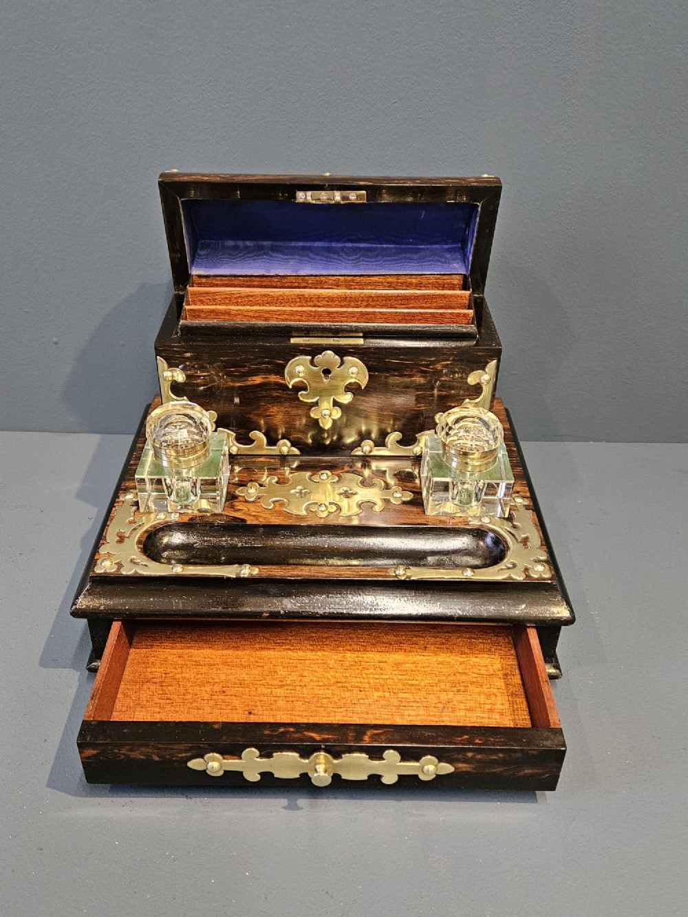 A Victorian coromandel wood stationery box and inkstand featuring gothic brass strapwork mounts, a domed lid, two glass inkwells, and a lower drawer with a key. View VII