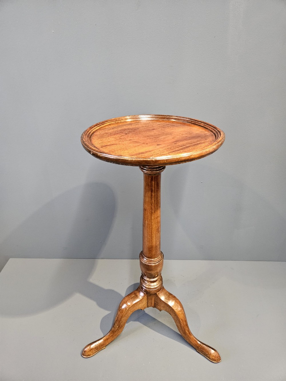 A Georgian mahogany wine table featuring a circular top with a moulded rim supported by a turned pedestal stem on tripod legs.