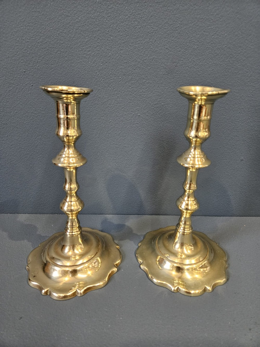 A pair of polished George III brass candlesticks with turned stems and scalloped petal-shaped bases.