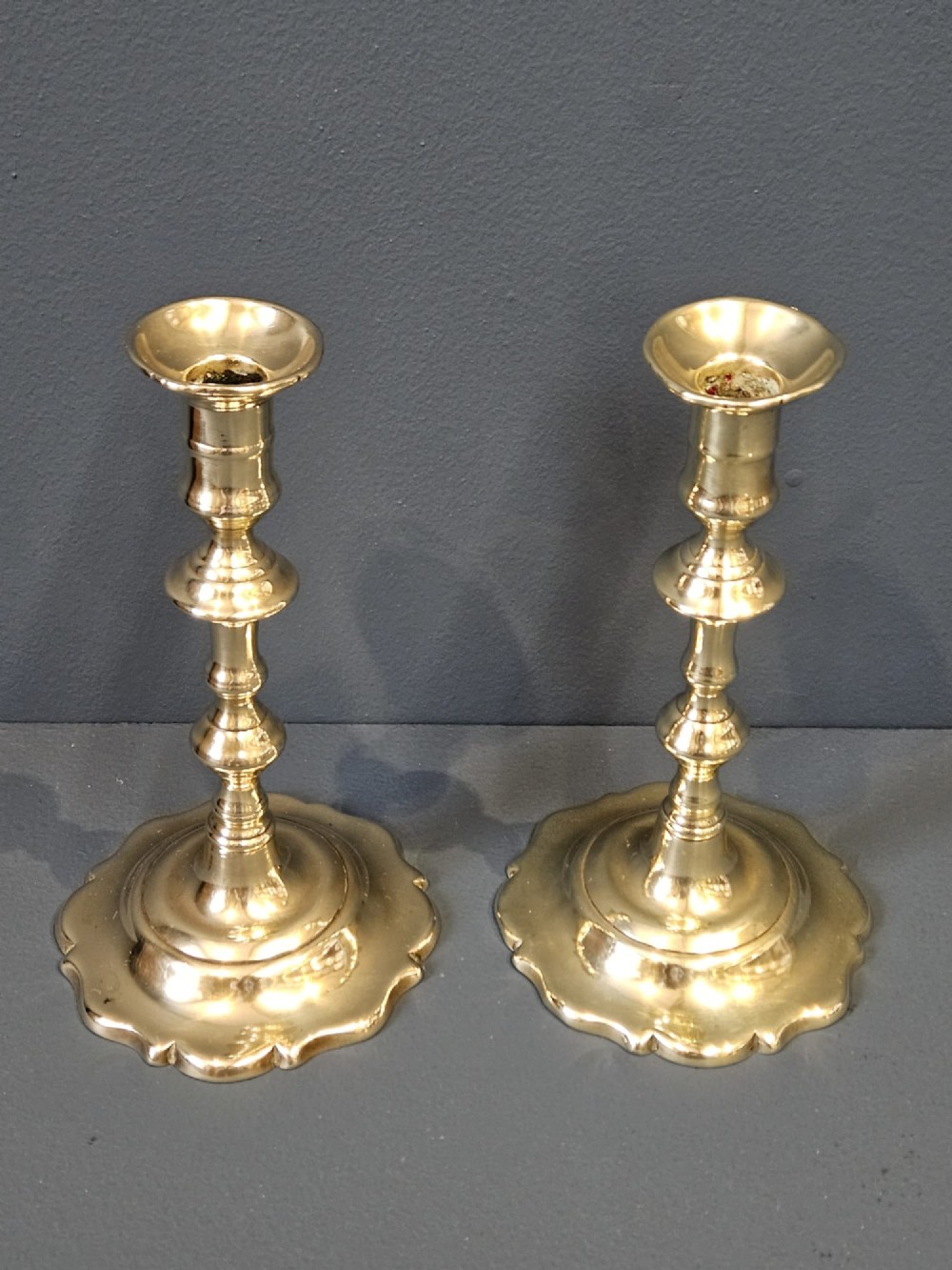 A pair of polished George III brass candlesticks with turned stems and scalloped petal-shaped bases. View II