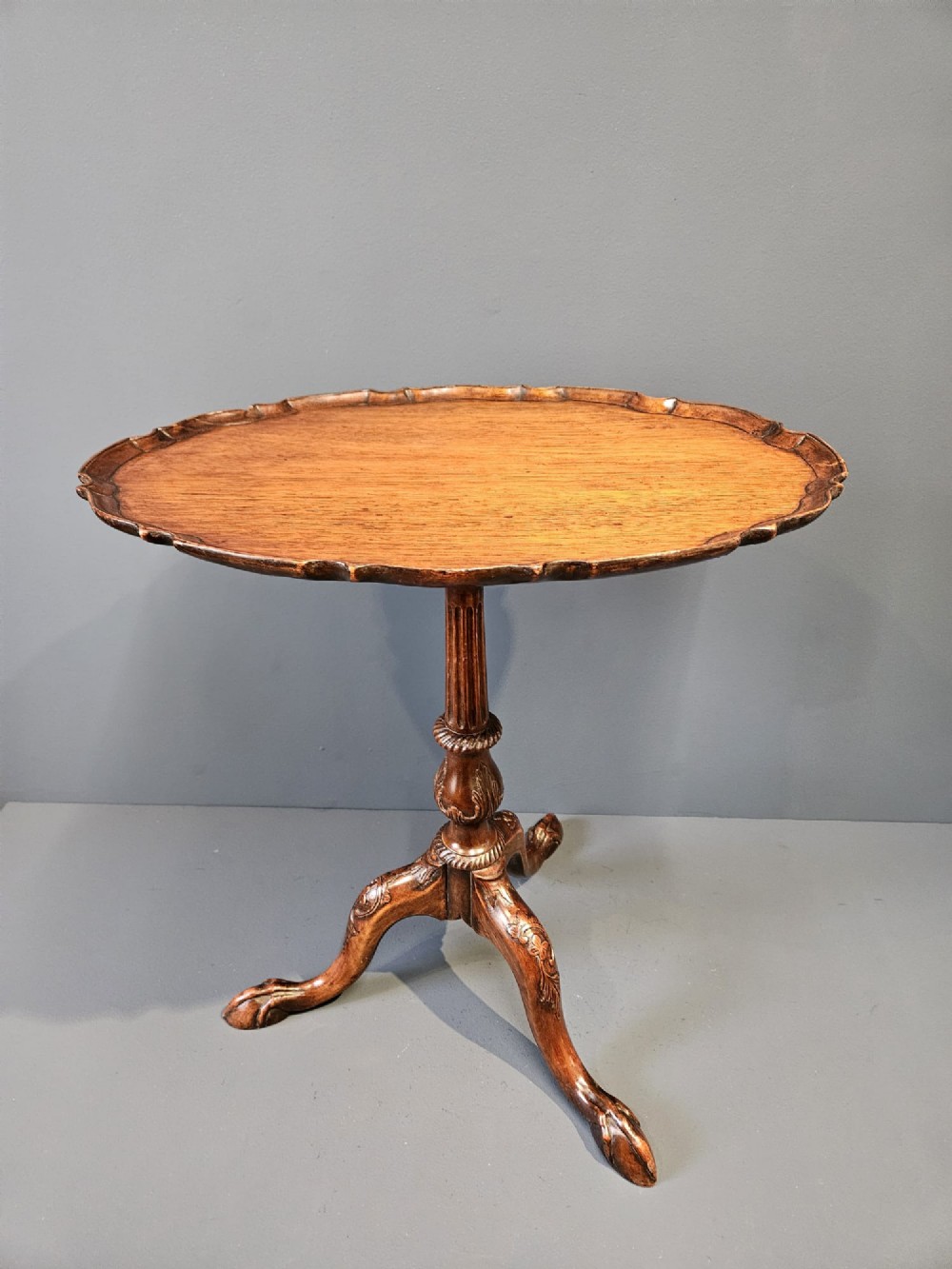 An Edwardian mahogany occasional table featuring an oval top with a raised piecrust edge, supported by a carved central pedestal and tripod cabriole legs.