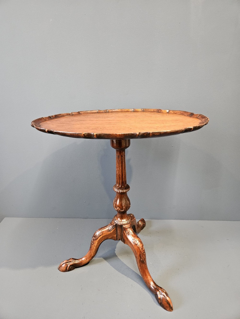 An Edwardian mahogany occasional table featuring an oval top with a raised piecrust edge, supported by a carved central pedestal and tripod cabriole legs. View II