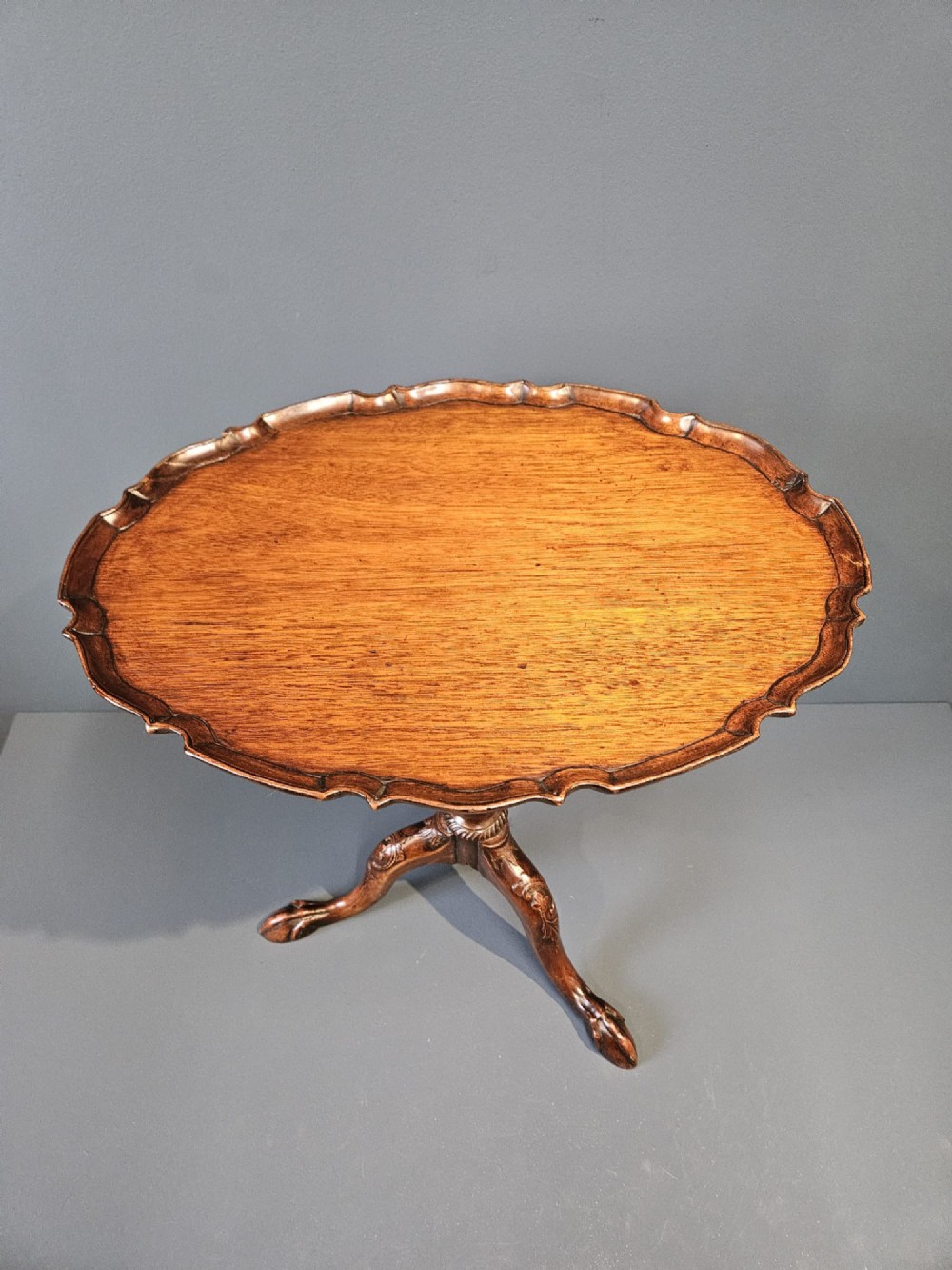 An Edwardian mahogany occasional table featuring an oval top with a raised piecrust edge, supported by a carved central pedestal and tripod cabriole legs. View III