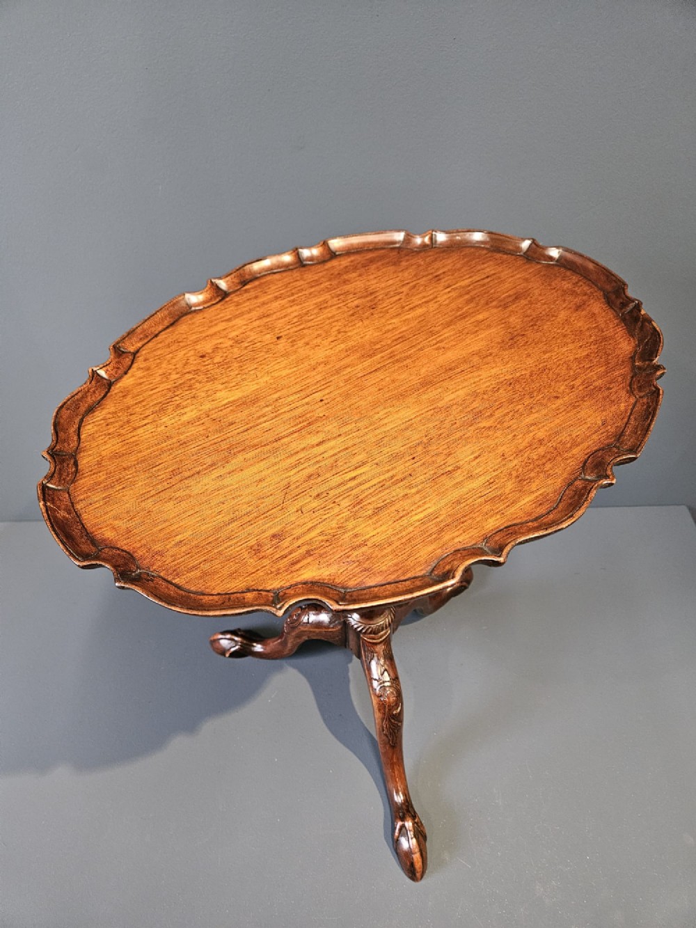 An Edwardian mahogany occasional table featuring an oval top with a raised piecrust edge, supported by a carved central pedestal and tripod cabriole legs. View VII