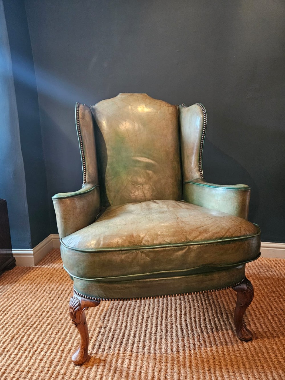 A George III wingback armchair in green leather upholstery featuring brass studding and carved walnut cabriole front legs.