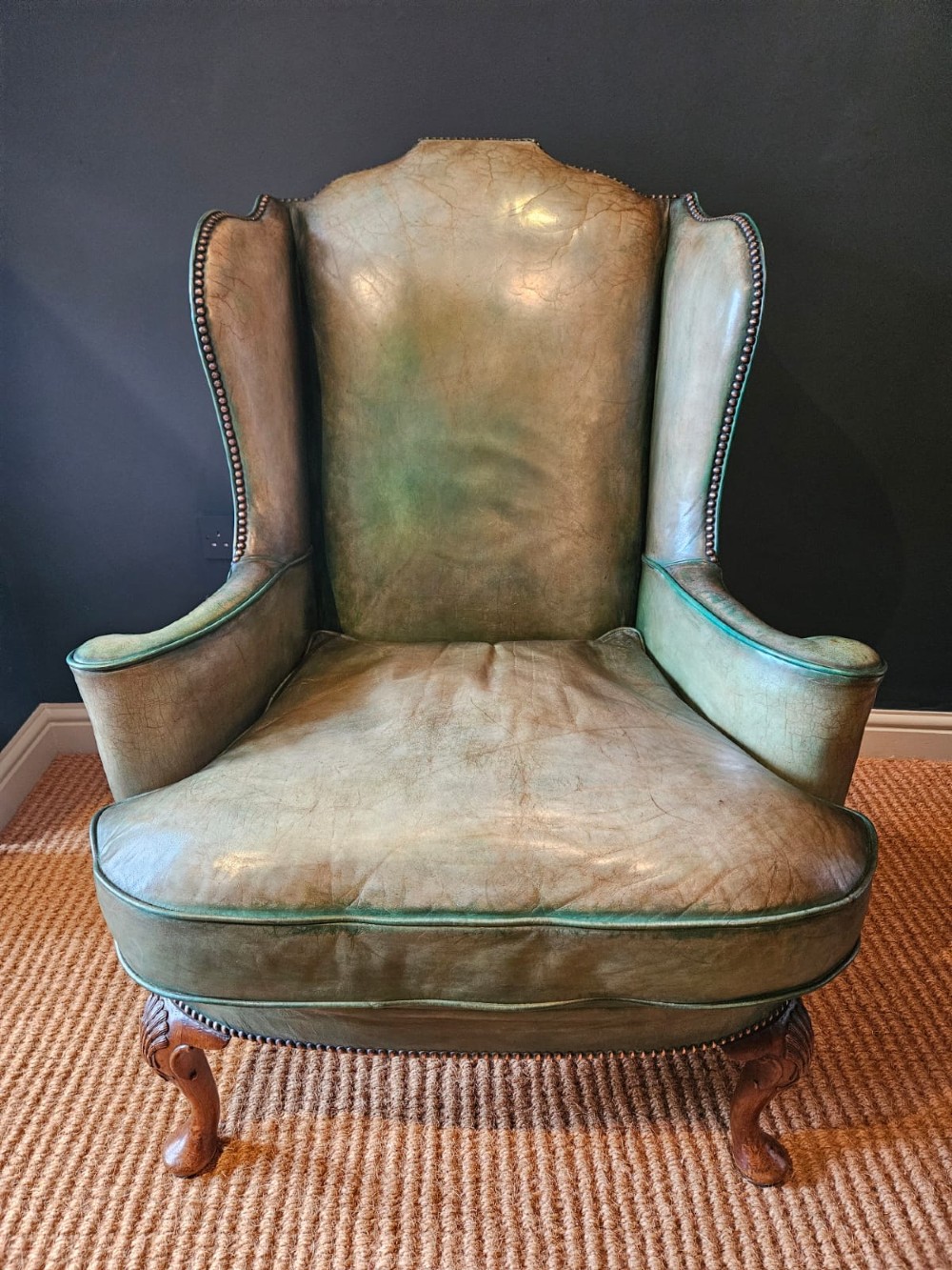 A George III wingback armchair in green leather upholstery featuring brass studding and carved walnut cabriole front legs. View II