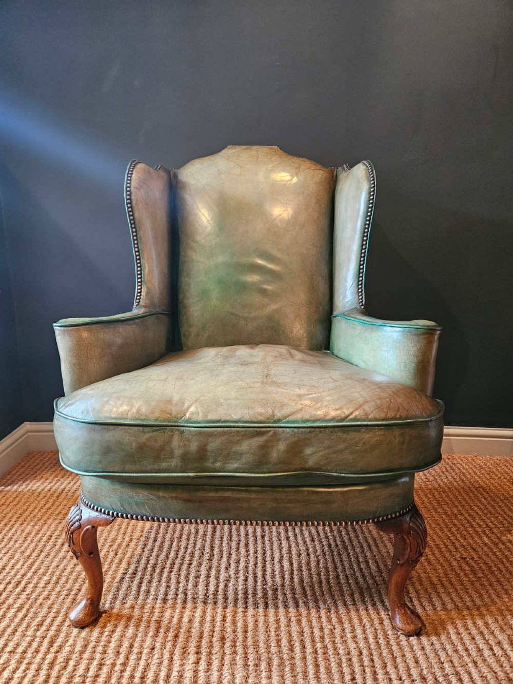 A George III wingback armchair in green leather upholstery featuring brass studding and carved walnut cabriole front legs. View III