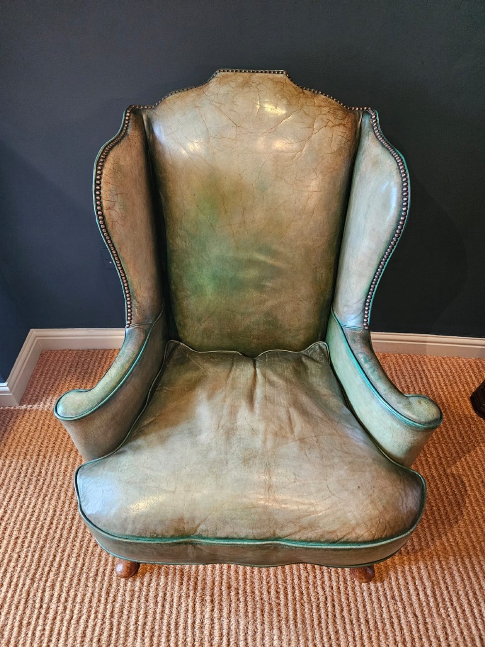 A George III wingback armchair in green leather upholstery featuring brass studding and carved walnut cabriole front legs. View V